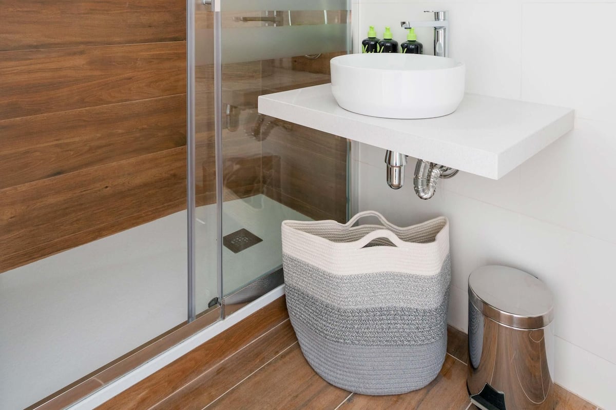 Un baño moderno con cabina de ducha de vidrio, un lavamanos blanco con espejo y suelo de madera.