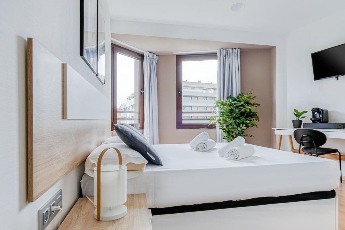 Una habitación de hotel con cama, escritorio, silla, televisor y ventana con cortinas.