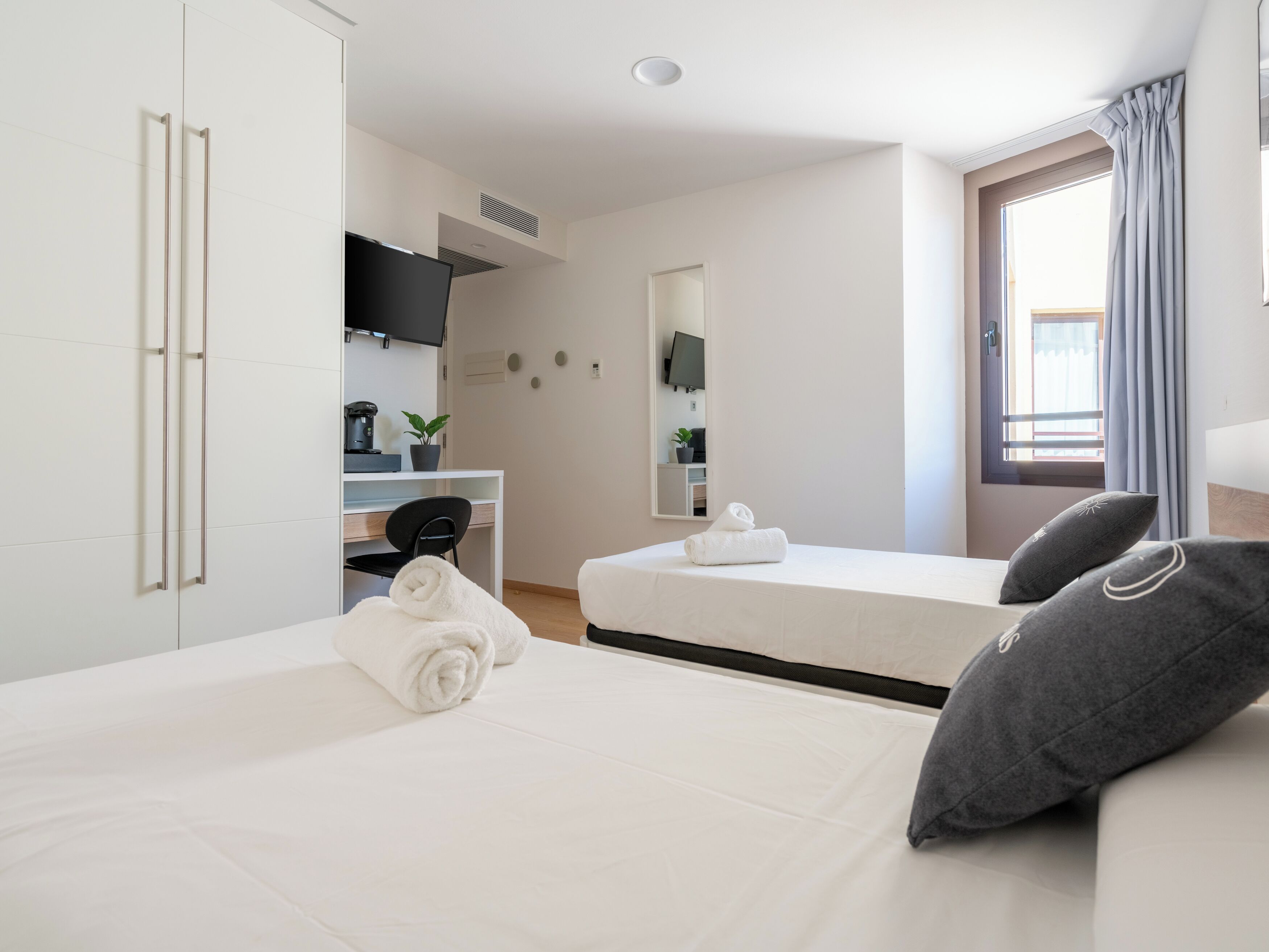 A hotel room with a bed, a desk, a chair, a TV, and a window with curtains.