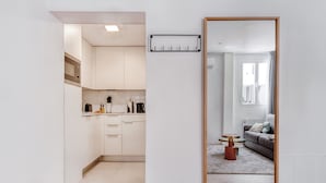 A modern kitchen with white cabinets, a wooden floor, and a large mirror reflecting a living room with a gray sofa and a small round table. - Limehome Madrid Calle Ave María (Madrid)