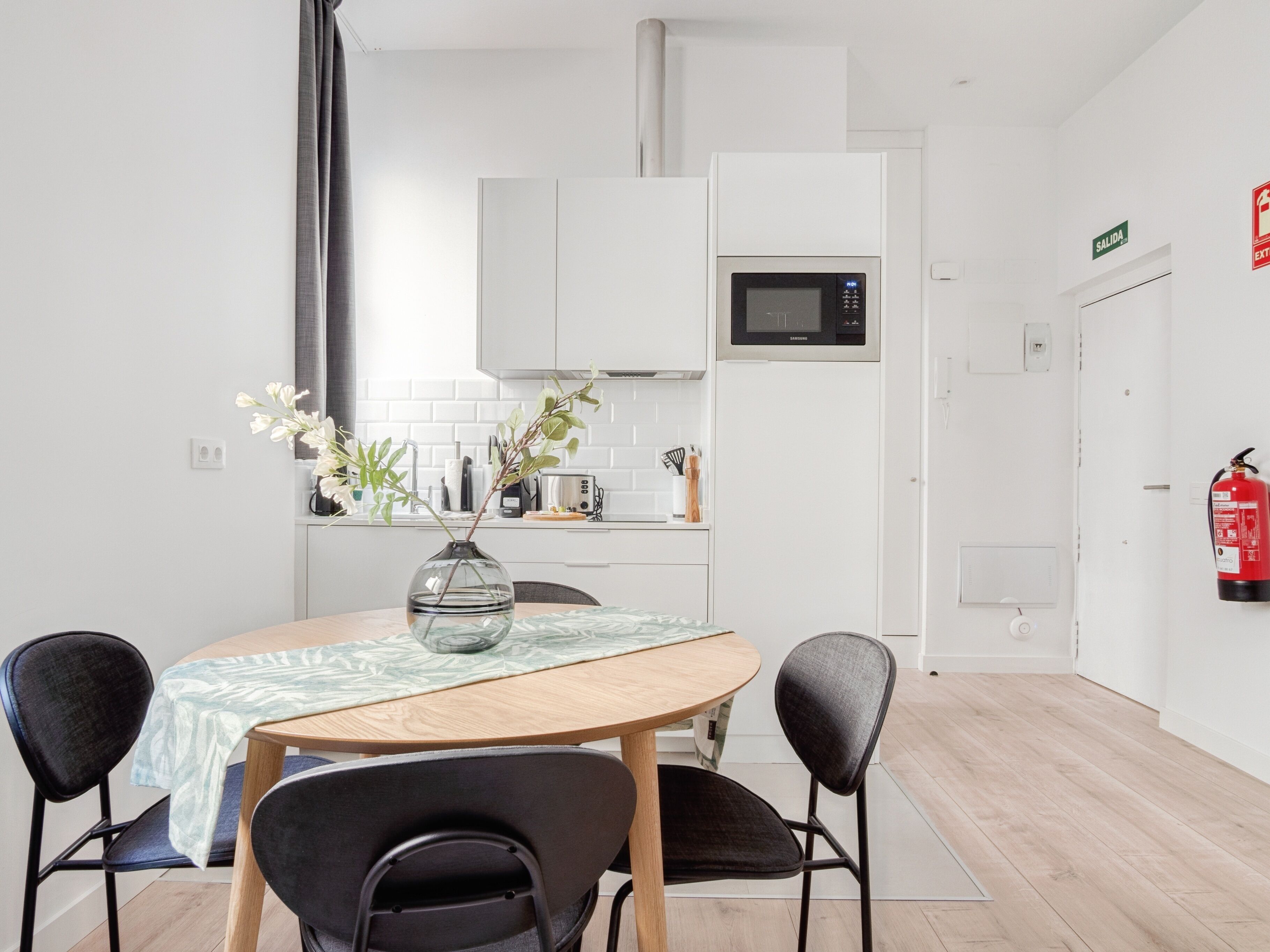 A modern kitchen with white cabinets, a microwave, and a dining area with a table and chairs.