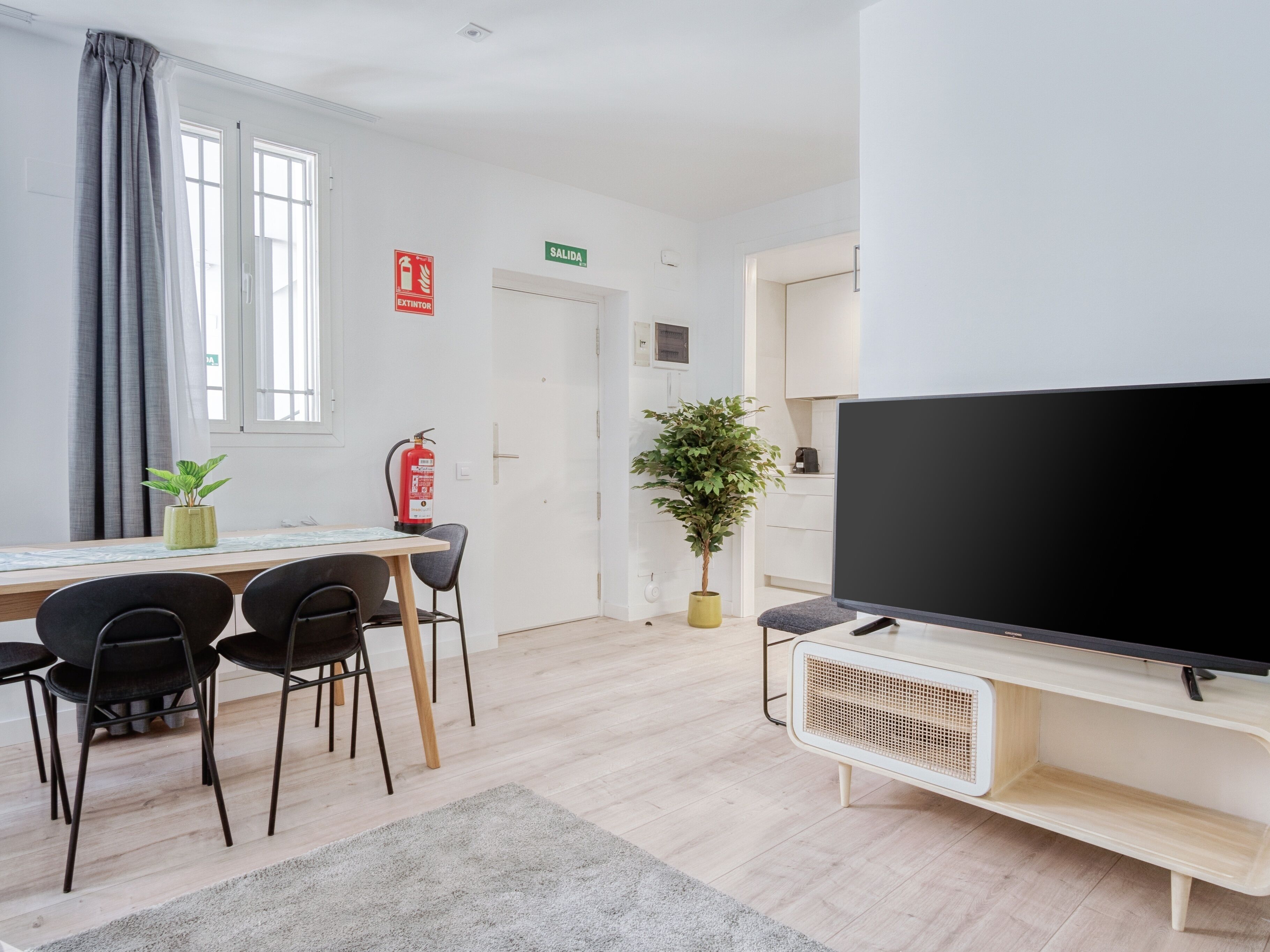 A modern room with a dining table, chairs, a television, and a fire extinguisher.