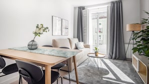 A modern living room with a sofa, a dining table with chairs, a small side table, and a potted plant. - Limehome Madrid Calle Ave María (Madrid)