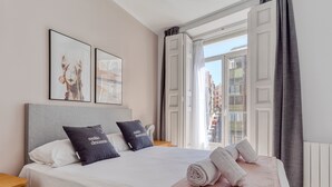 A neatly made bed with pillows, a bedside table, and a window with curtains. - Limehome Madrid Calle Ave María (Madrid)