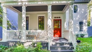 Une maison à deux étages avec un porche soutenu par des colonnes, une porte rouge et un petit jardin.