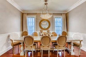 A dining room with a large table, six chairs, a chandelier, and a mirror on the wall.