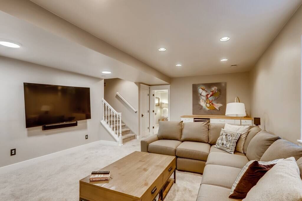 A modern living room with a flat-screen TV, a wooden coffee table, a beige sofa, and a staircase leading to another room.