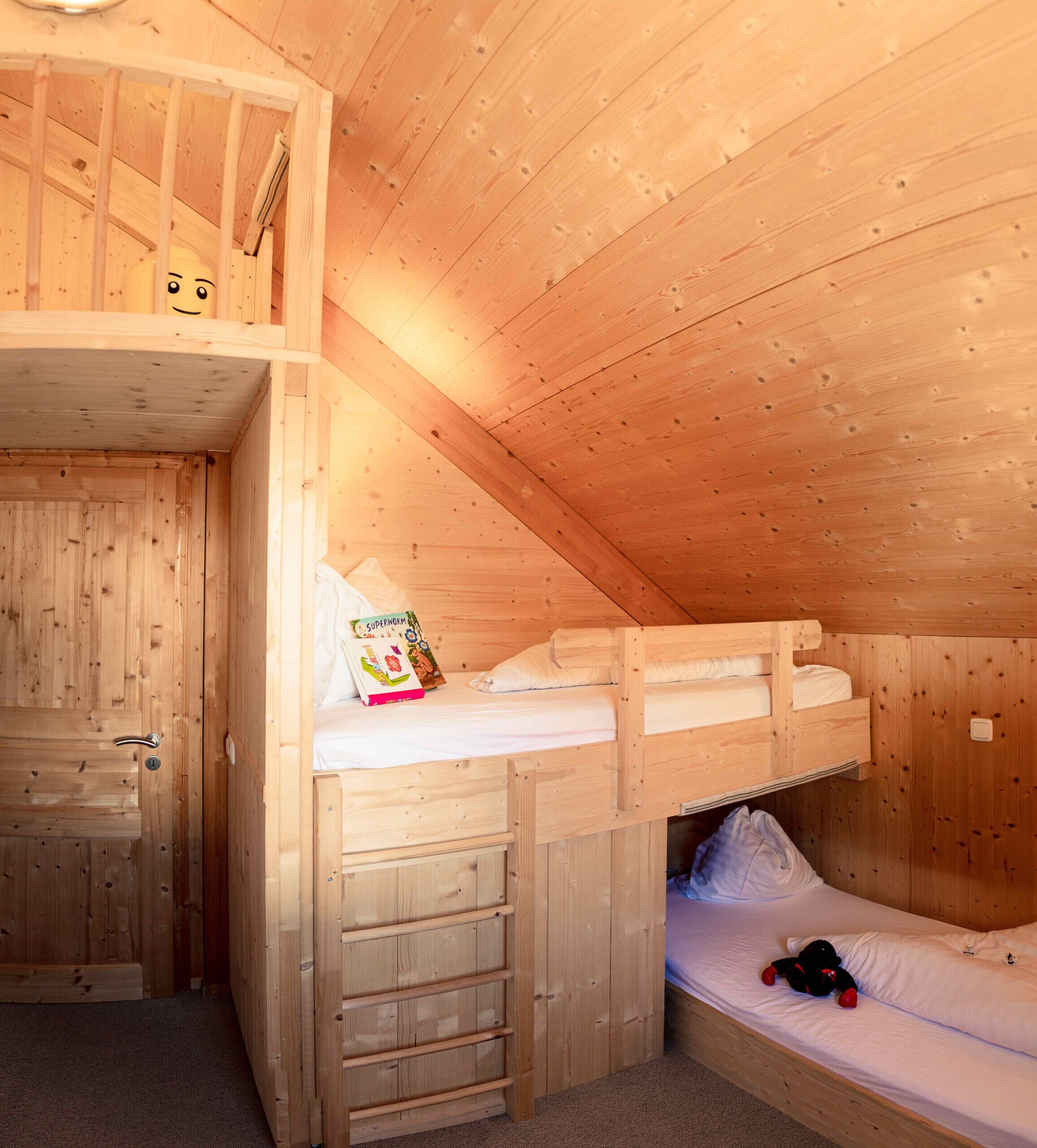 A wooden cabin room with bunk beds, a wooden door, and a small ladder.