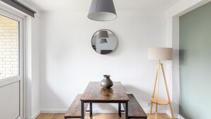 Et spiseområde med et træbord, en vase, et rundt spejl og en gulvlampe.