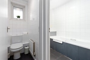 A bathroom with a toilet, a small window with a plant, a bathtub, and a radiator. -  2 Bed Flat with Garden in Canonbury (London)