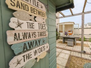 Un letrero de madera con motivos marítimos y texto, sujeto a un edificio verde.