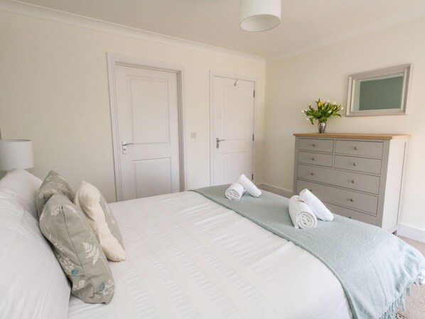 A bedroom with a bed, two doors, a dresser, a lamp, and a vase with flowers.