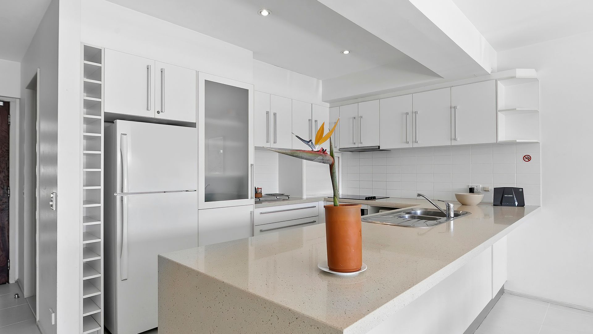 Une cuisine moderne avec des meubles blancs, un réfrigérateur en acier inoxydable et un plan de travail agrémenté d’une plante en pot.