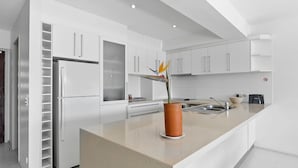 A modern kitchen with white cabinets, a stainless steel refrigerator, and a countertop with a potted plant. - Driftwood 5 Noosaville (Noosaville)