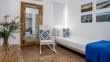 Une pièce avec un canapé blanc, un fauteuil à bascule, une table en bois ornée d’un vase de fleurs, un grand miroir et quatre tableaux encadrés accrochés au mur.
