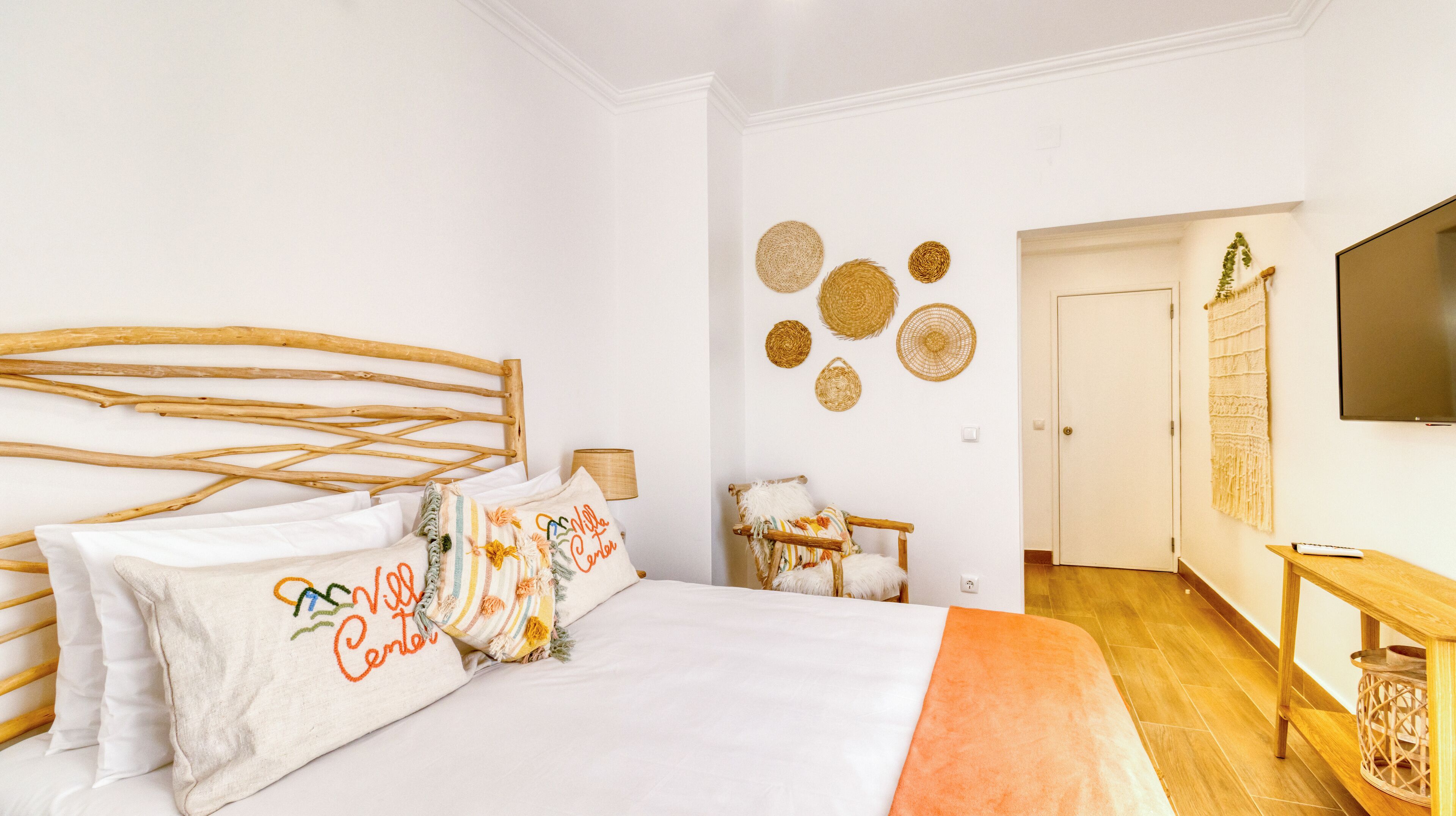 A bedroom with a wooden bed, white walls, and a TV on the wall.