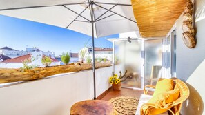 A balcony with a view of buildings, a wicker chair, a small table, and a basket with sunflowers. - Villa Center (Grandola)
