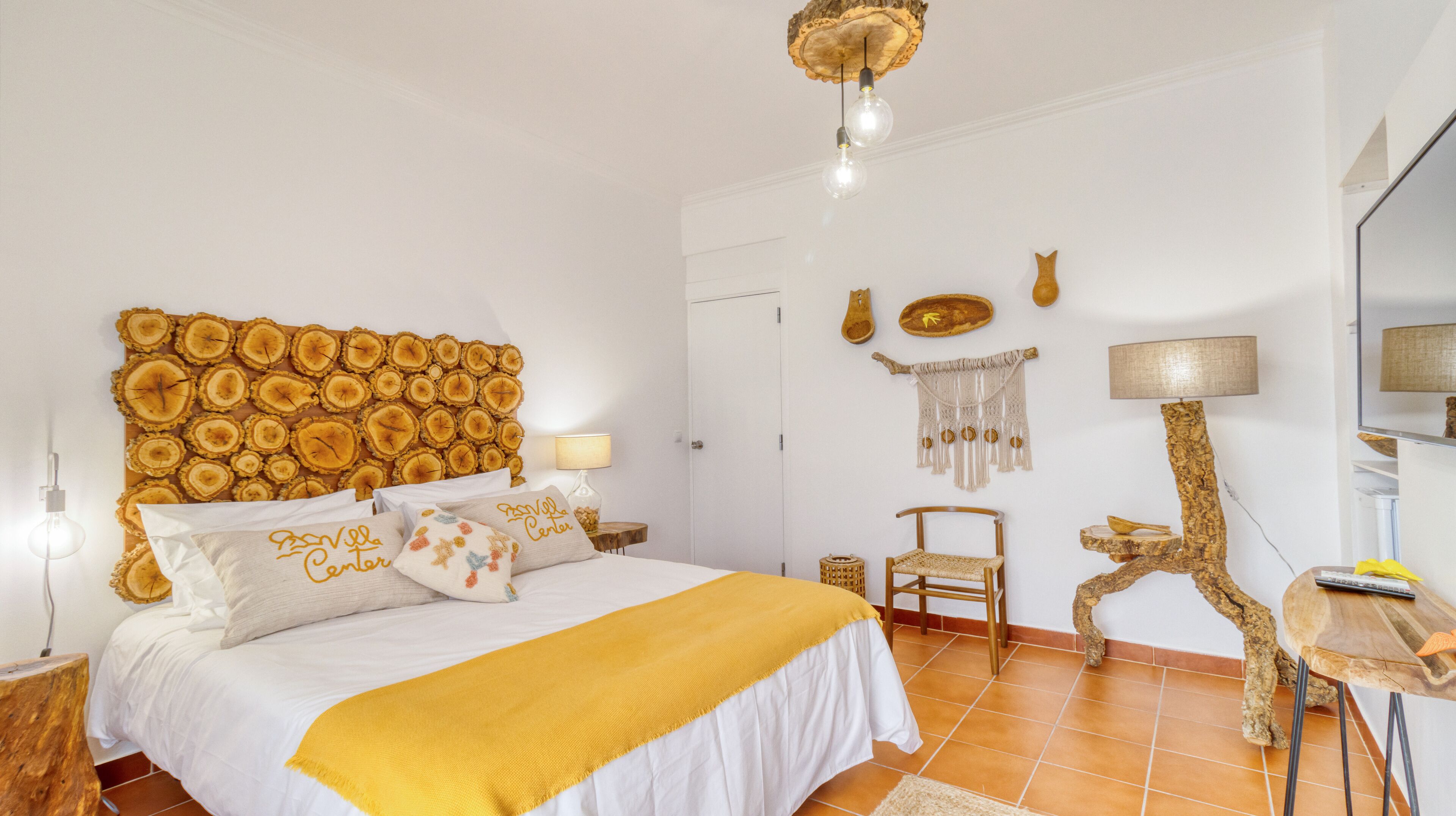 A bedroom with a bed, a wooden headboard, a bedside table, a lamp, a chair, and a desk.