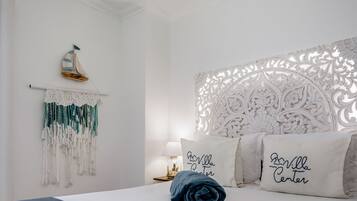Une chambre à coucher bien aménagée, avec un lit, des coussins décoratifs, une décoration murale en macramé et un objet décoratif représentant un voilier.