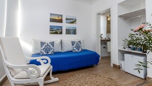 Ein Schlafzimmer mit einem Bett, einem Sessel, einem kleinen Kühlschrank und einer Pflanze.