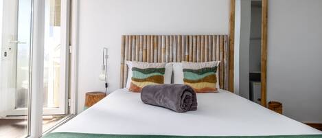 Un lit bien fait, avec une couverture verte, des coussins colorés et une tête de lit en bois.