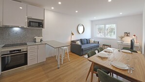 Eine moderne Küche mit Mikrowelle, Backofen und einer Arbeitsplatte aus Granit. Es gibt einen Essbereich mit einem Holztisch, gedeckt für vier Personen, und ein graues Sofa im Wohnzimmer.
