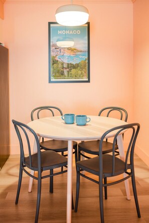 Un'area pranzo con un tavolo rotondo, quattro sedie, due tazze blu e un quadro incorniciato di Monaco sulla parete.