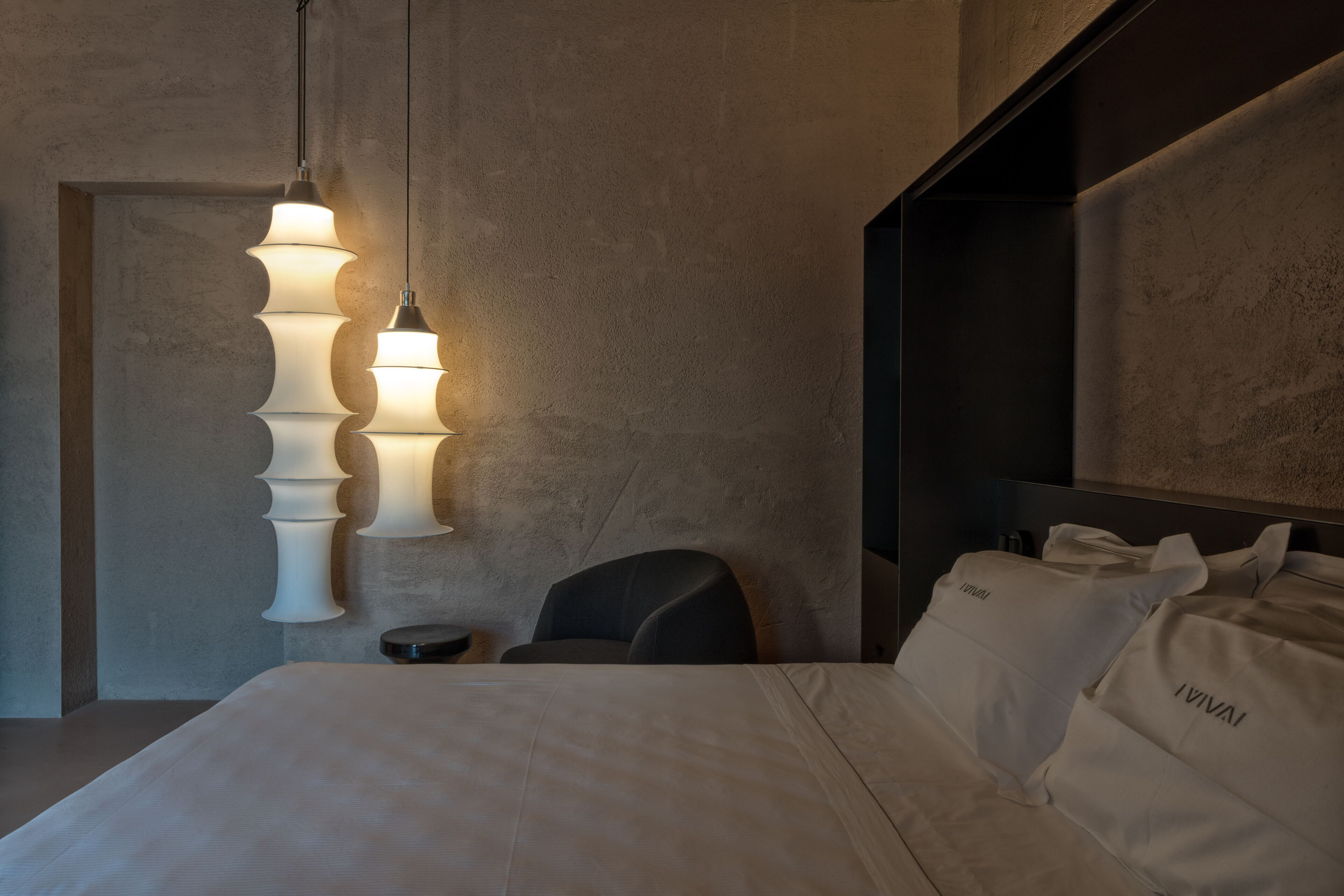 Une chambre d’hôtel moderne avec un grand lit, une chaise et un luminaire mural original.