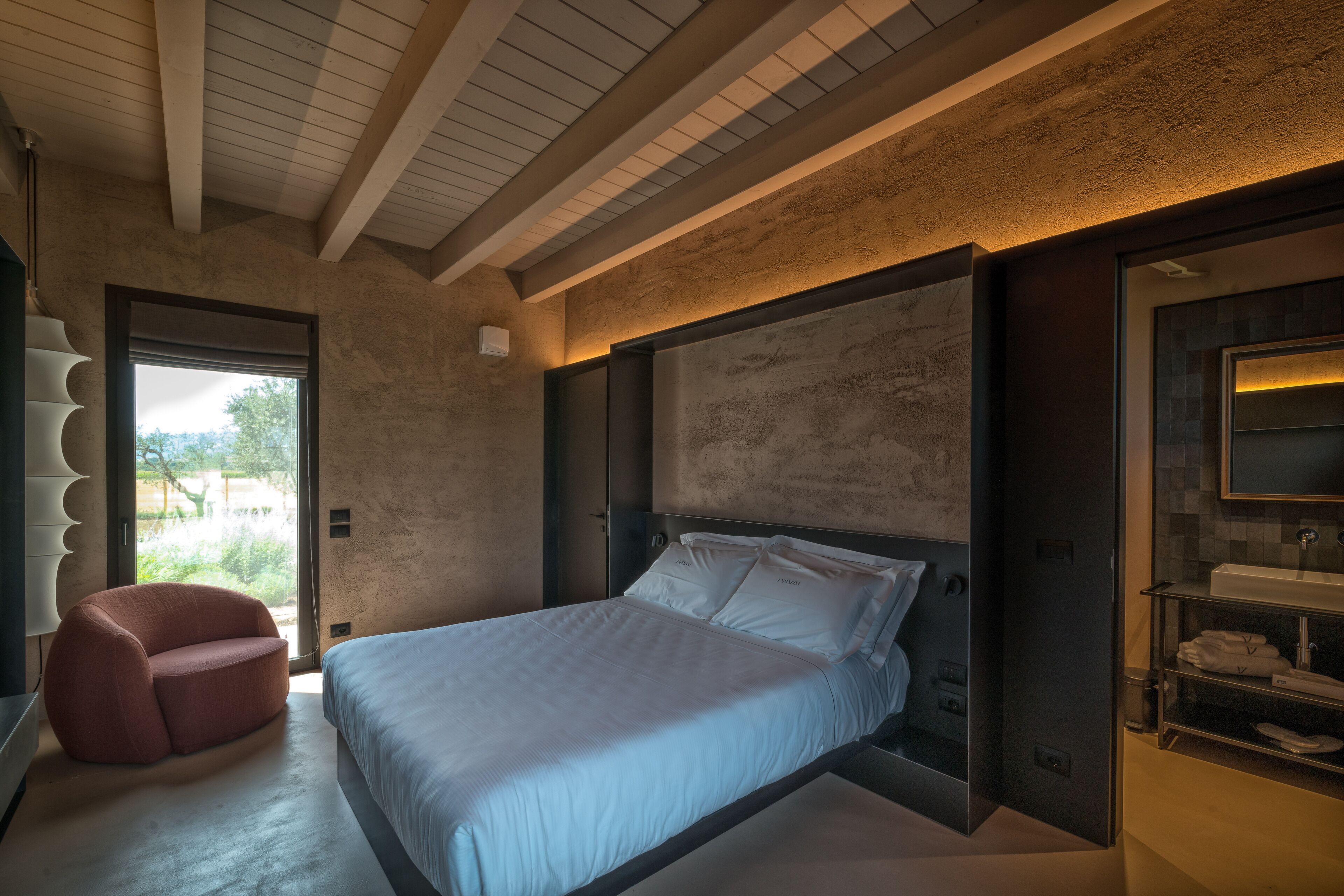 Ein modernes Schlafzimmer mit einem großen Bett, einer Sitzecke und einem Badezimmer mit Waschtisch und Regalen.