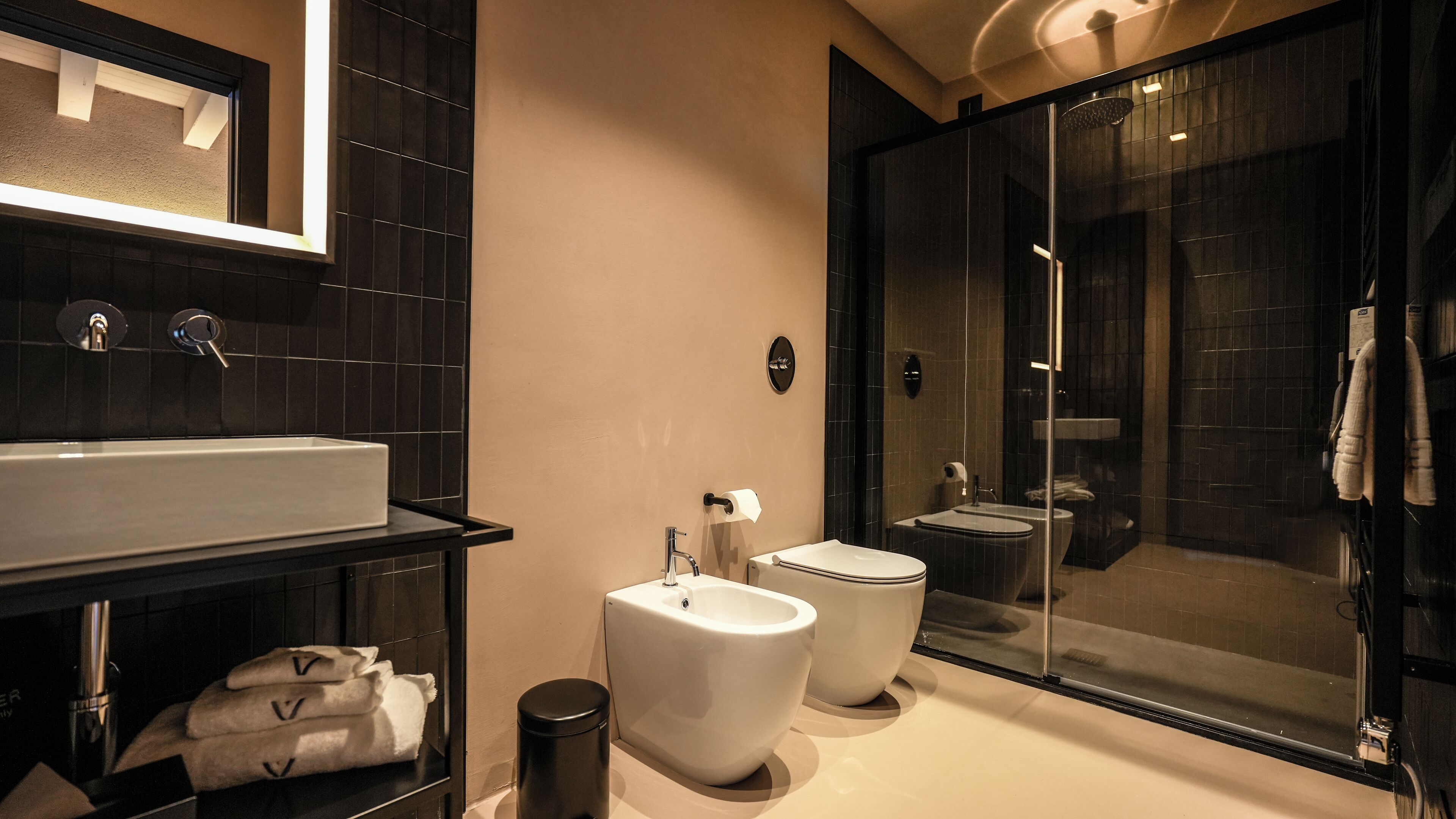 Un baño moderno con un lavabo grande, dos bidés, una ducha con mampara de vidrio y un espejo sobre el lavabo.