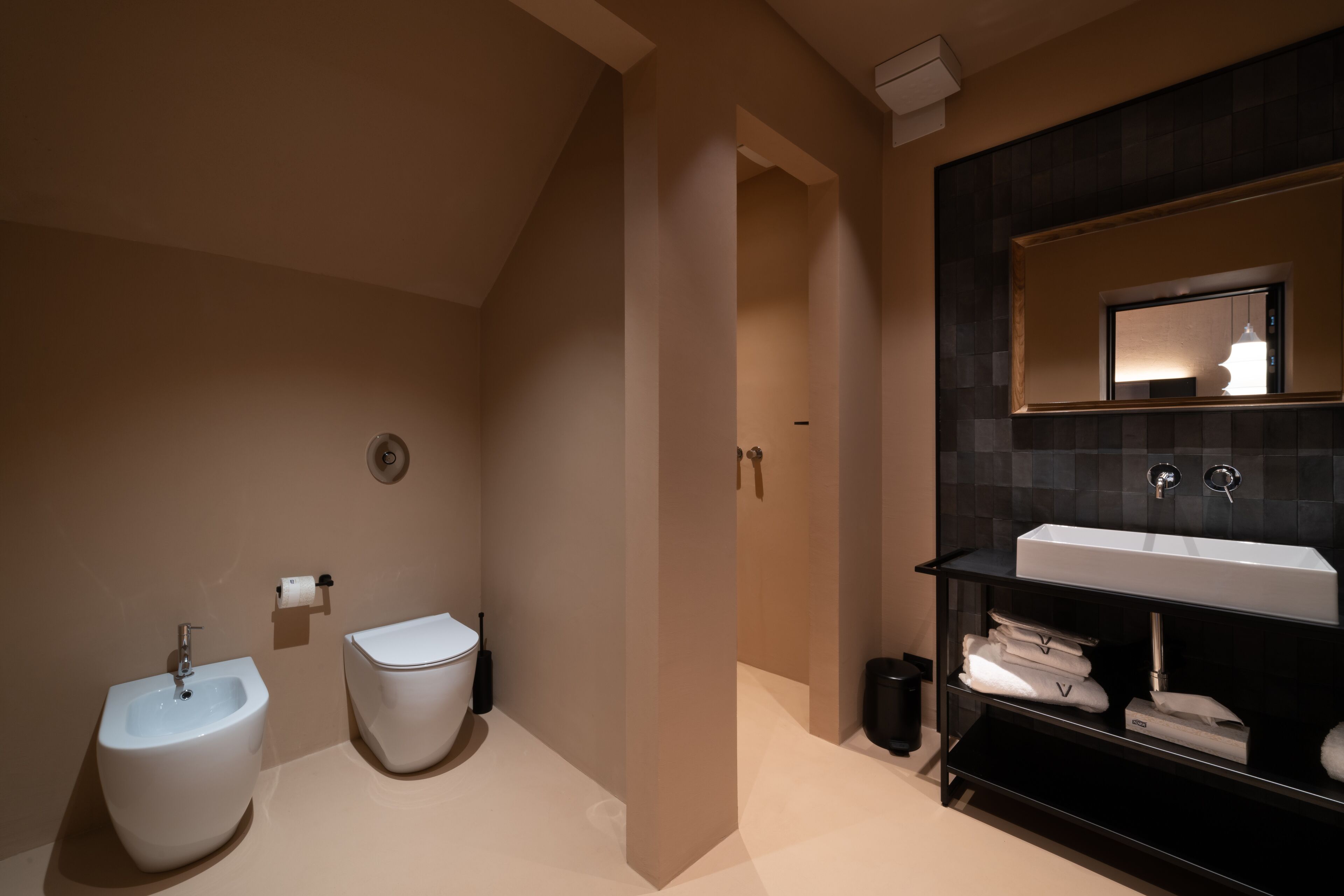A modern bathroom with a bidet, toilet, and a large sink with a mirror above it.