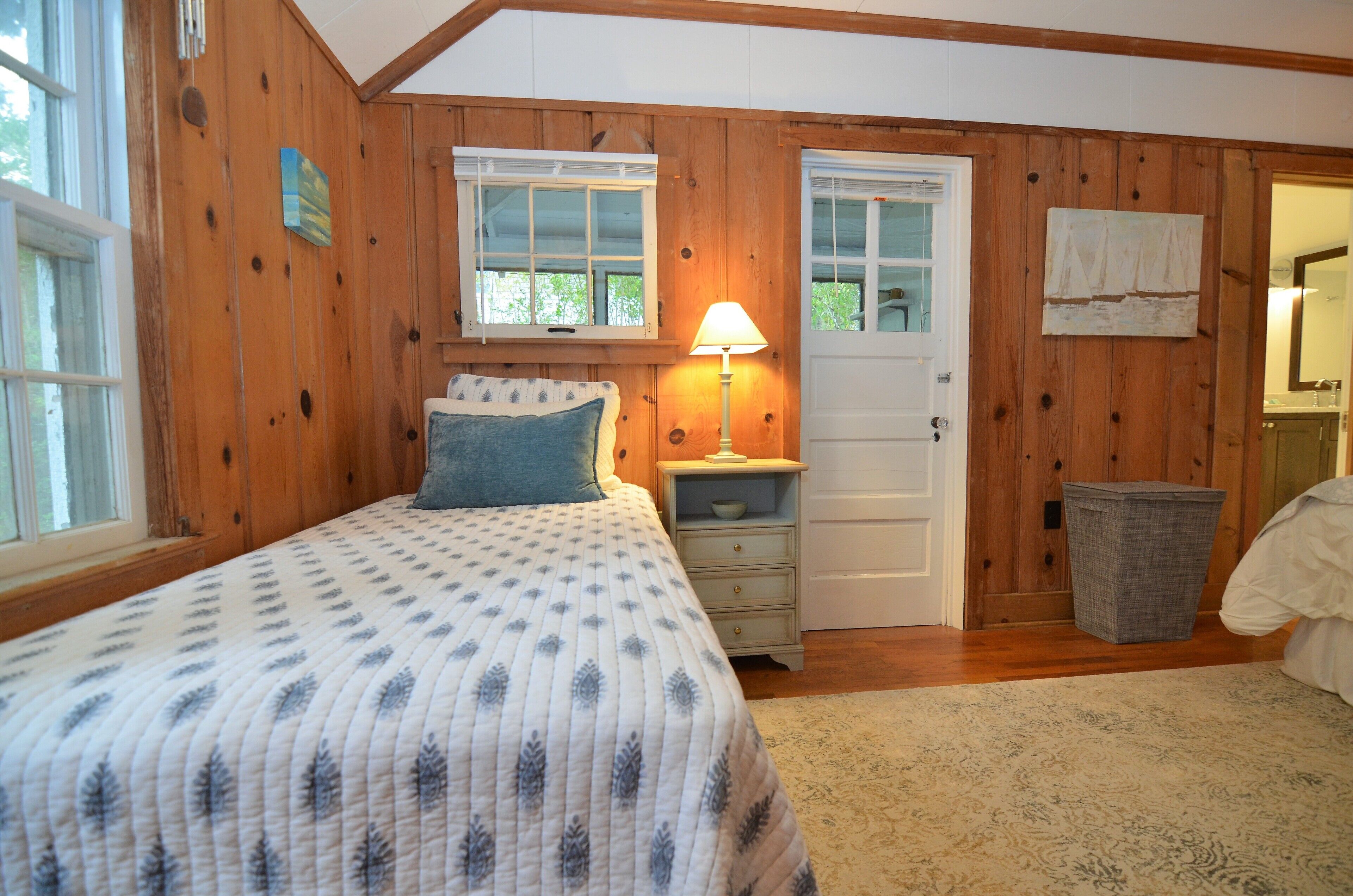 A bedroom with a bed, a nightstand, a lamp, a door, and a window.