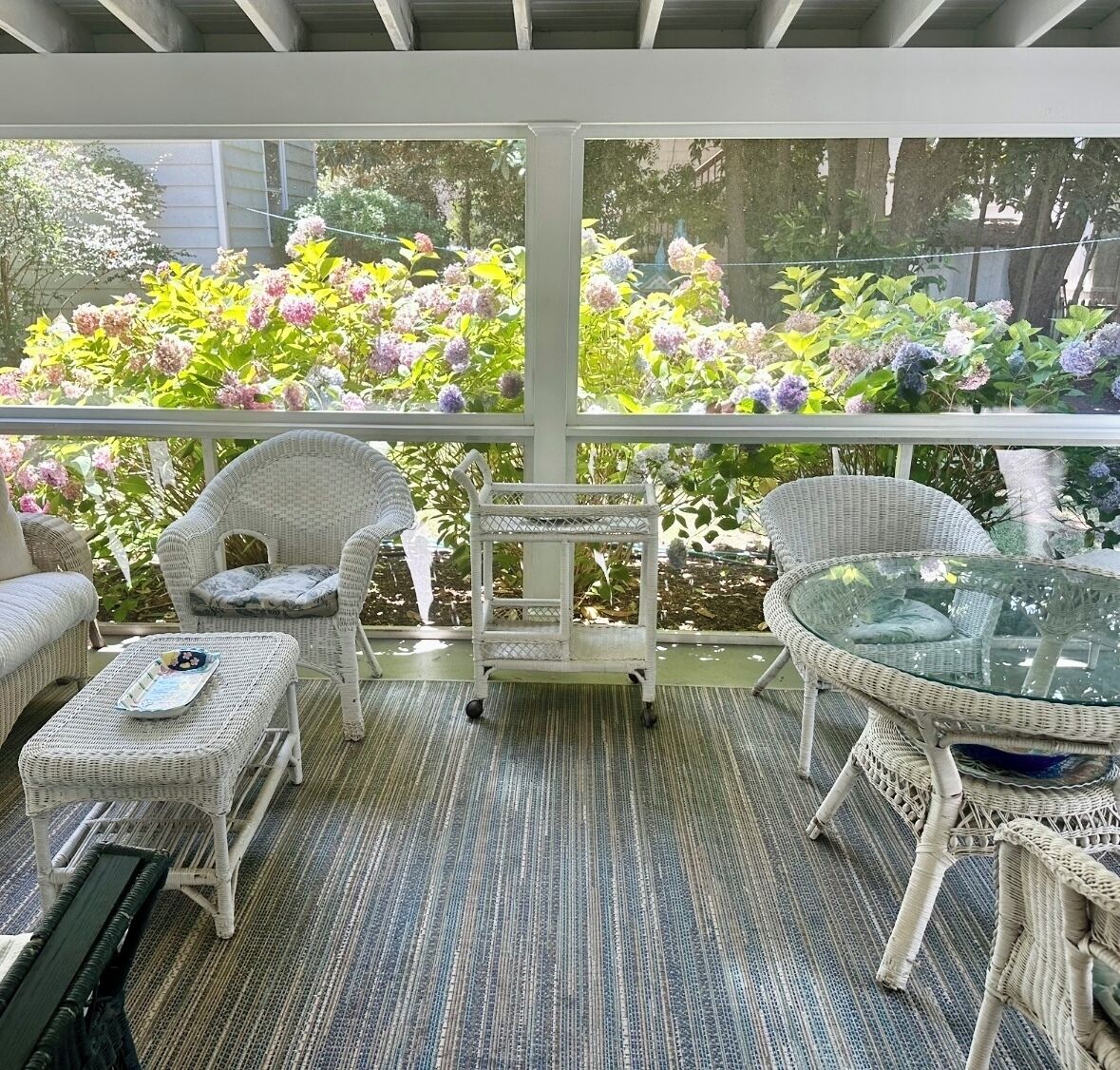 Een overdekt terras met rieten meubels, een glazen tafel en een kleine kar.