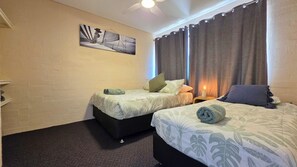 Ein Hotelzimmer mit zwei Betten, einem Bild an der Wand, einem Deckenventilator und einem Nachttisch mit Lampe.
