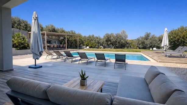 Un área junto a la piscina con un sofá, sillones de descanso y una mesa con una planta.