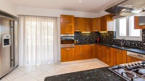 Una cocina moderna con armarios de madera, encimera negra, electrodomésticos de acero inoxidable y una ventana con cortinas.