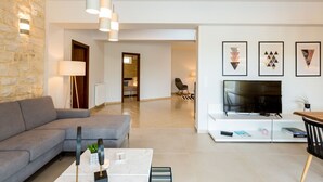 Una sala moderna con un sofá gris, una mesita de centro, un televisor sobre un mueble blanco y una pared de piedra.