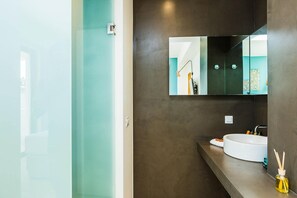 A modern bathroom with a large mirror, a round sink, and a glass shower enclosure.