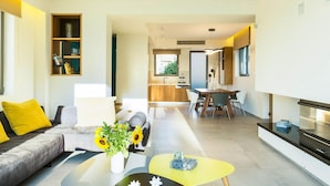 A modern living room with a sofa, coffee table, and a dining area in the background. - Villa Amelia I Free Mini van Private Pool (Chania)