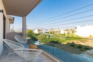 A balcony with white wicker chairs, a view of a road, and buildings in the background.
