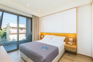 A hotel room with a bed, a nightstand with a lamp, a sliding glass door to the balcony, and a view of the city. - Villa Amelia I Free Mini van Private Pool (Chania)