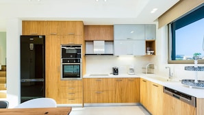 A modern kitchen with wooden cabinets, a black refrigerator, a built-in oven, a dishwasher, and a large window. - Villa Amelia I Free Mini van Private Pool (Chania)