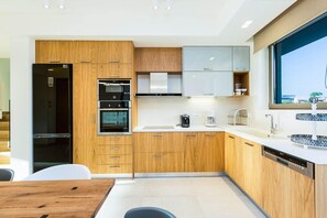 Een moderne keuken met houten kastjes, een zwarte koelkast, een inbouwoven, een vaatwasser en een groot raam.