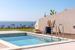 A swimming pool with a view of the sea, a lounge area with a blue towel, and a cactus plant on the wall. - Villa Vista I Free Heated Pool Dazzling Seaview (Kissamos)