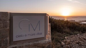 Placa com 'Cielo e mare villas' e vista do mar ao pôr do sol.