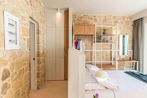 A modern bedroom with a stone wall, a wardrobe, a bed with pillows, a desk with a chair, and a shelving unit with a plant. - Villa Vista I Free Heated Pool Dazzling Seaview (Kissamos)