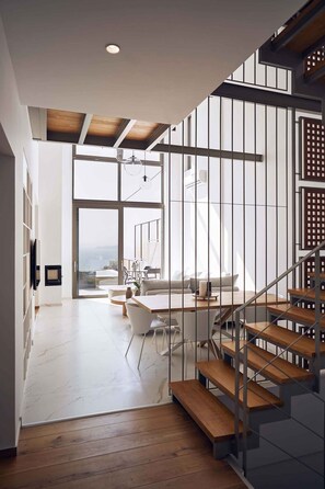 Un vaste espace de vie agrémenté d’un escalier en bois, de grandes fenêtres et d’une vue sur l’extérieur.
