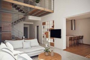 Un salon moderne avec un canapé blanc, une table basse ronde, un téléviseur et un escalier.