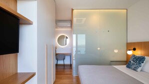 A modern hotel room with a bed, a TV, a desk, and a bathroom with a glass door. - Omnia Villa I - Heated Pool Stunning Seaview (Chania)