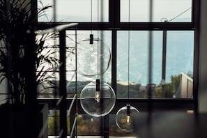 A modern interior with large windows, a potted plant, and three spherical glass pendant lights. - Omnia Villa I - Heated Pool Stunning Seaview (Chania)